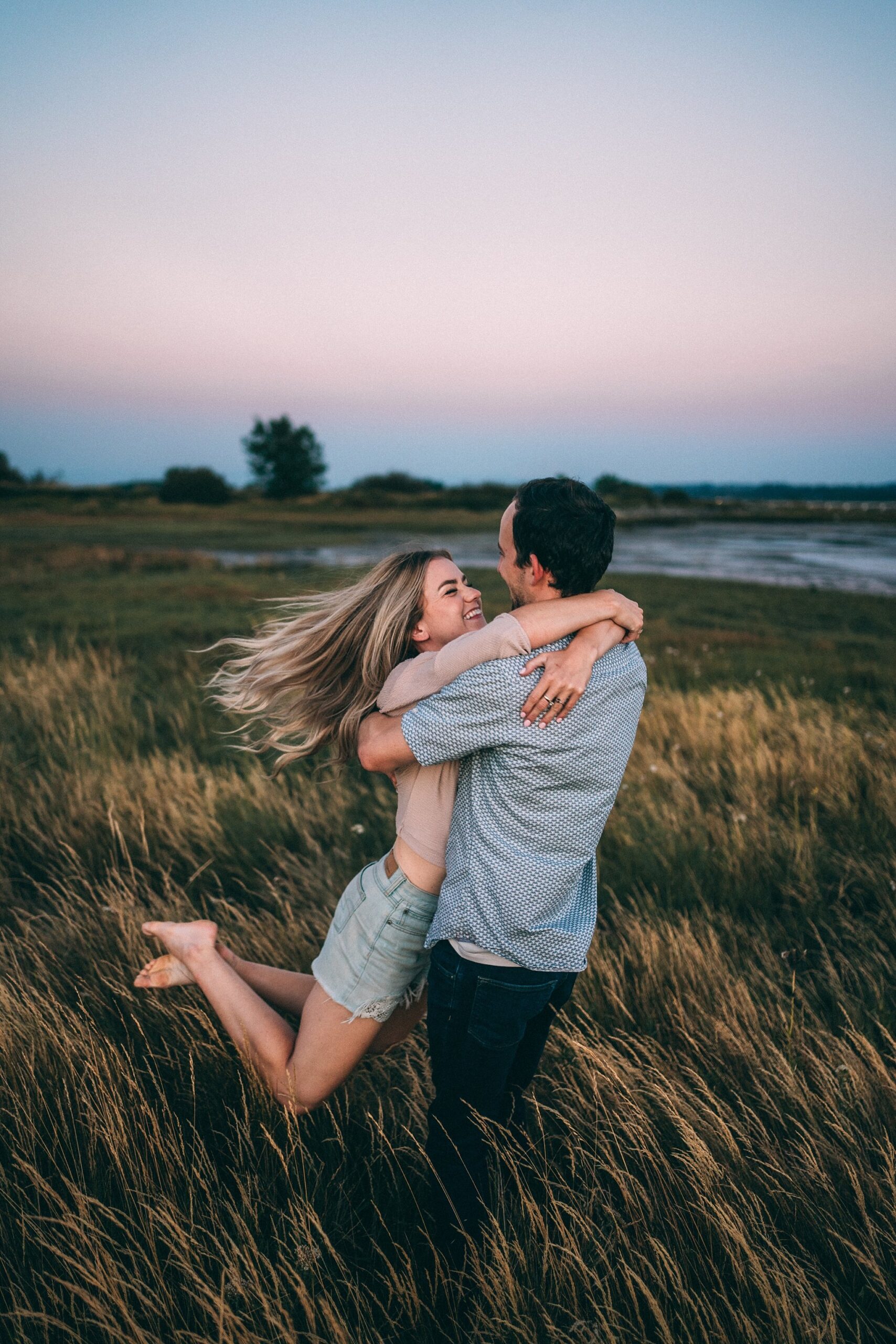 man swinging woman in his arms in long grass