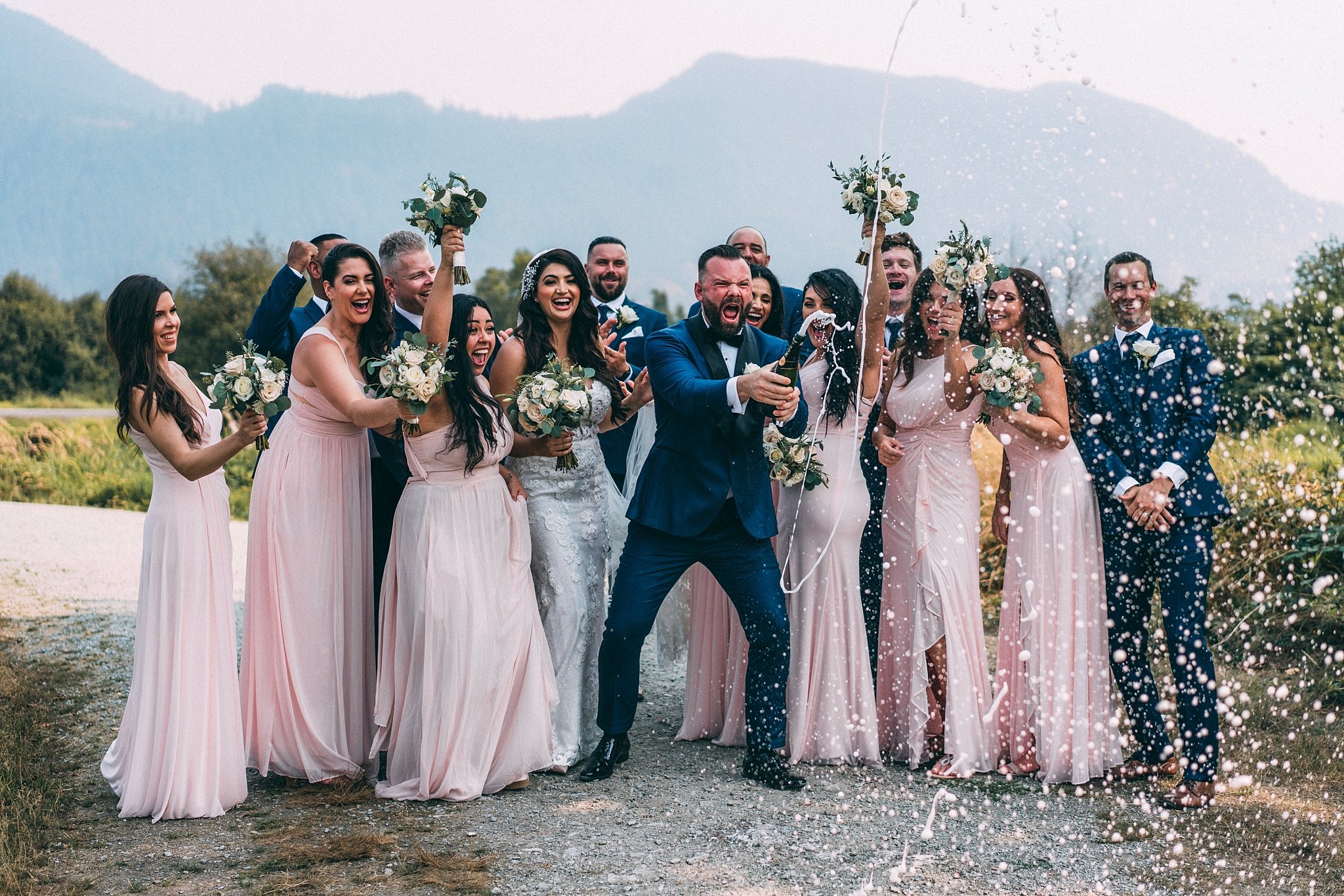 groom shaking bottle of champagne with wedding party cheering