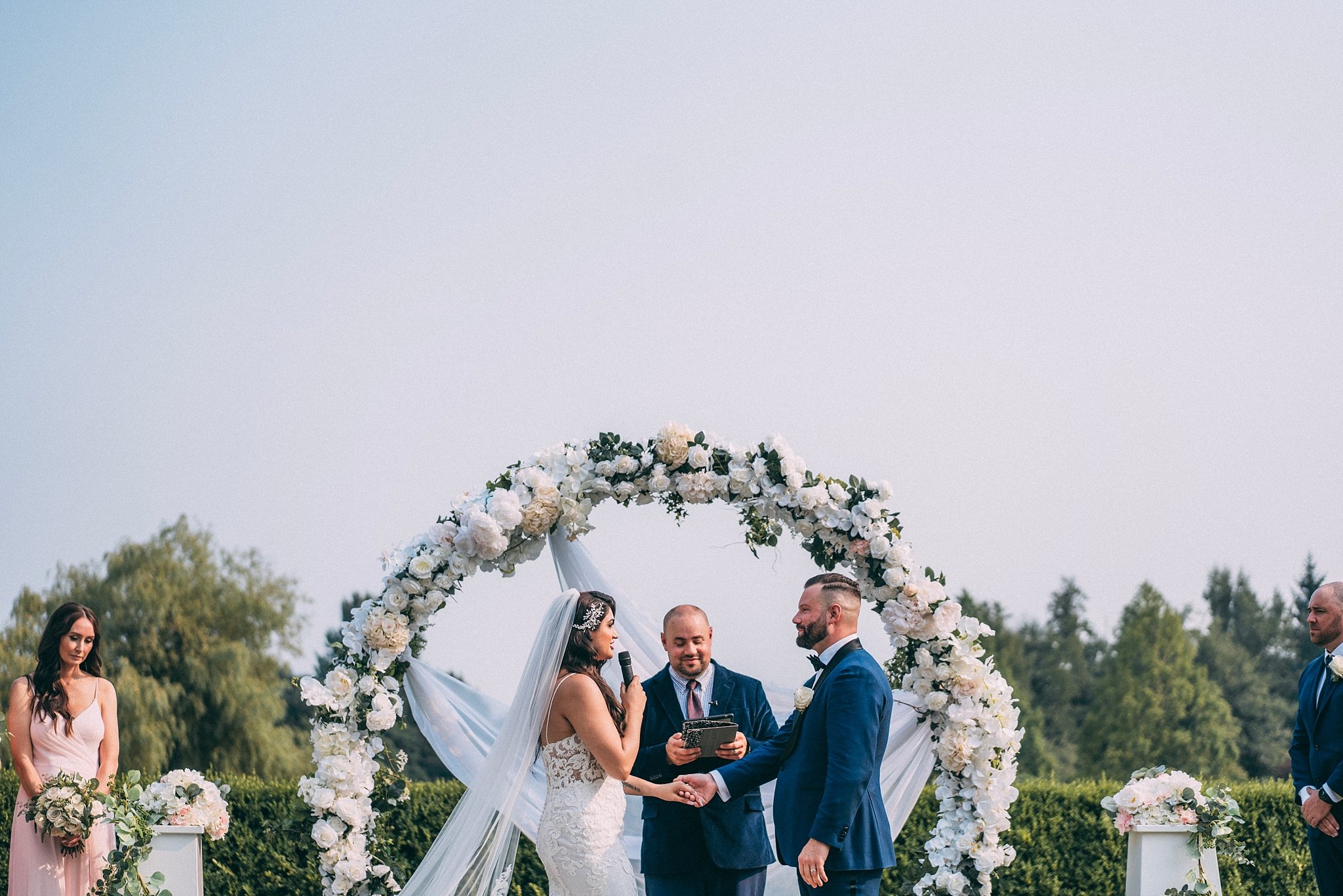 bride reading vows to groom during wedding ceremony under floral arch