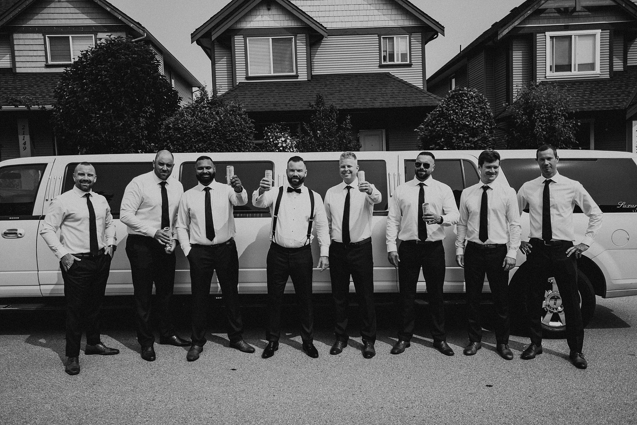 groom and groomsmen toasting in front of white limo