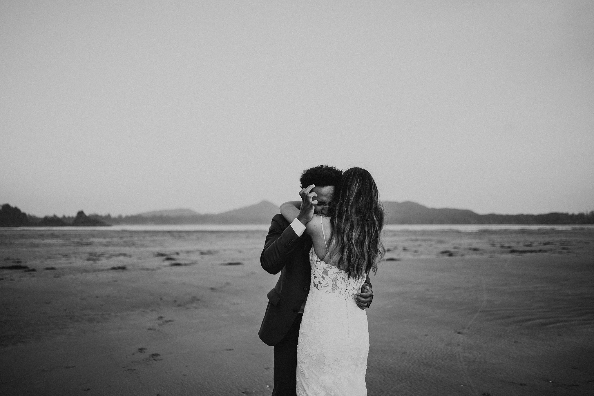 black and white photo of groom crying while bride hugs him