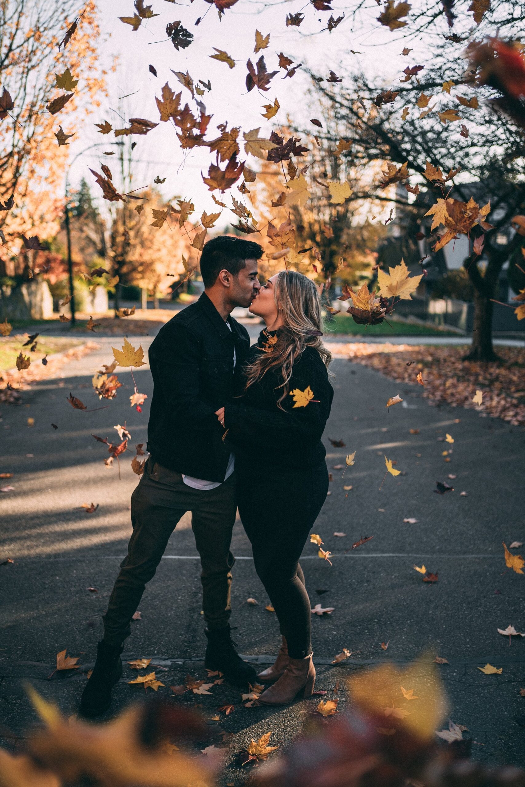 autumn leaves falling while couple kisses in middle of street
