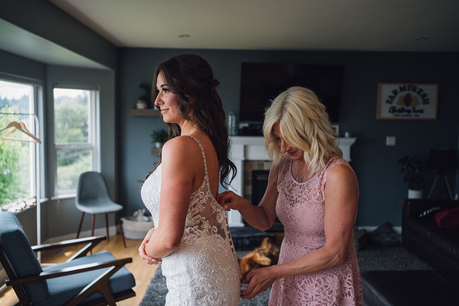 bride getting ready for wedding day putting on wedding dress with mom