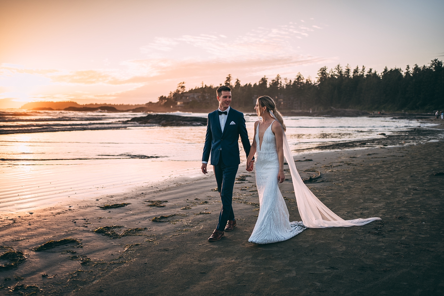 bride and groom walking holding hands  on beach in tofino