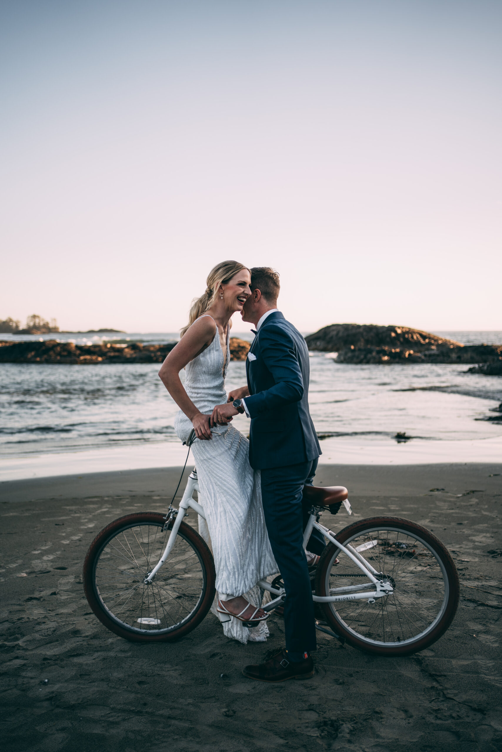 bride laughing with groom riding bike rented from wickaninnish inn on chesterman beach 