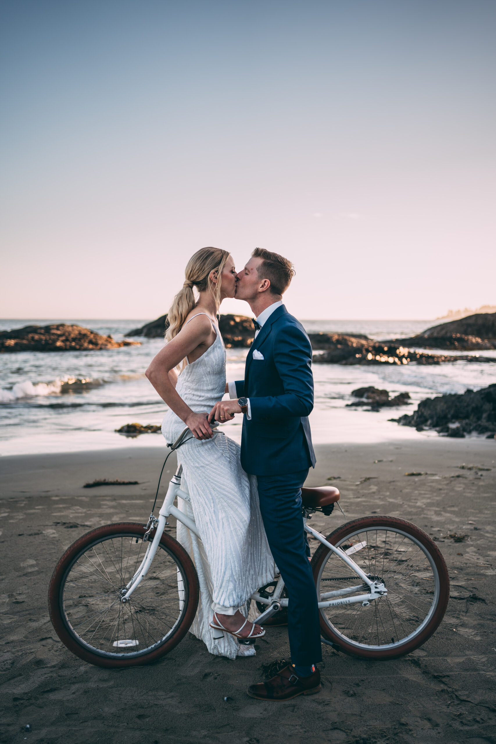bride and groom kissing while riding bike on beach