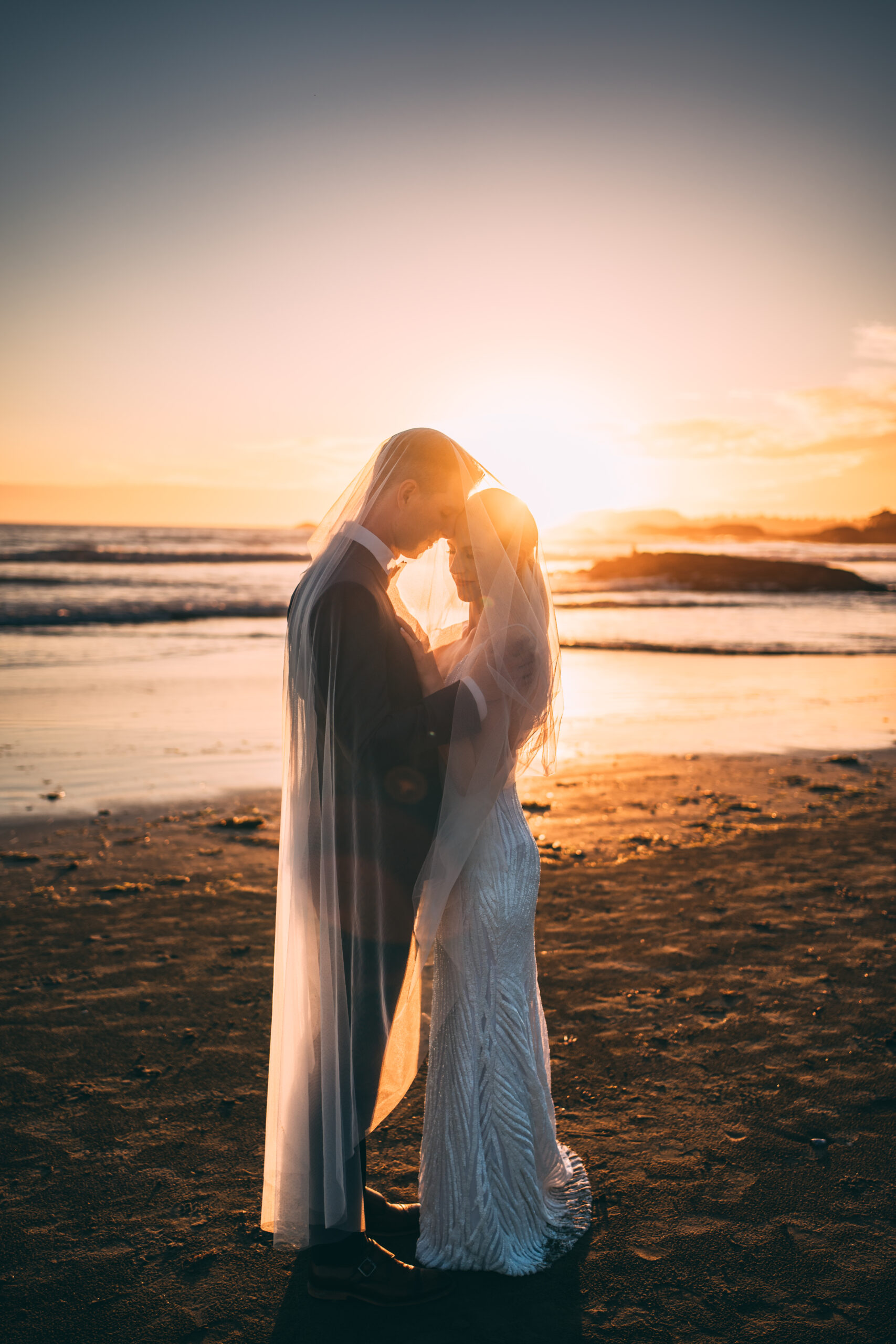 bride and groom elopement at sunset in tofino under wedding veil
