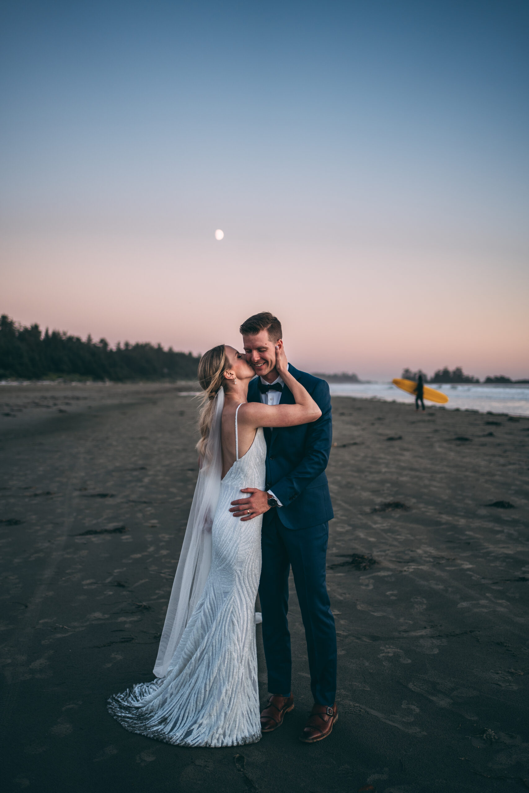 bride and groom elopement in tofino with surfer in background