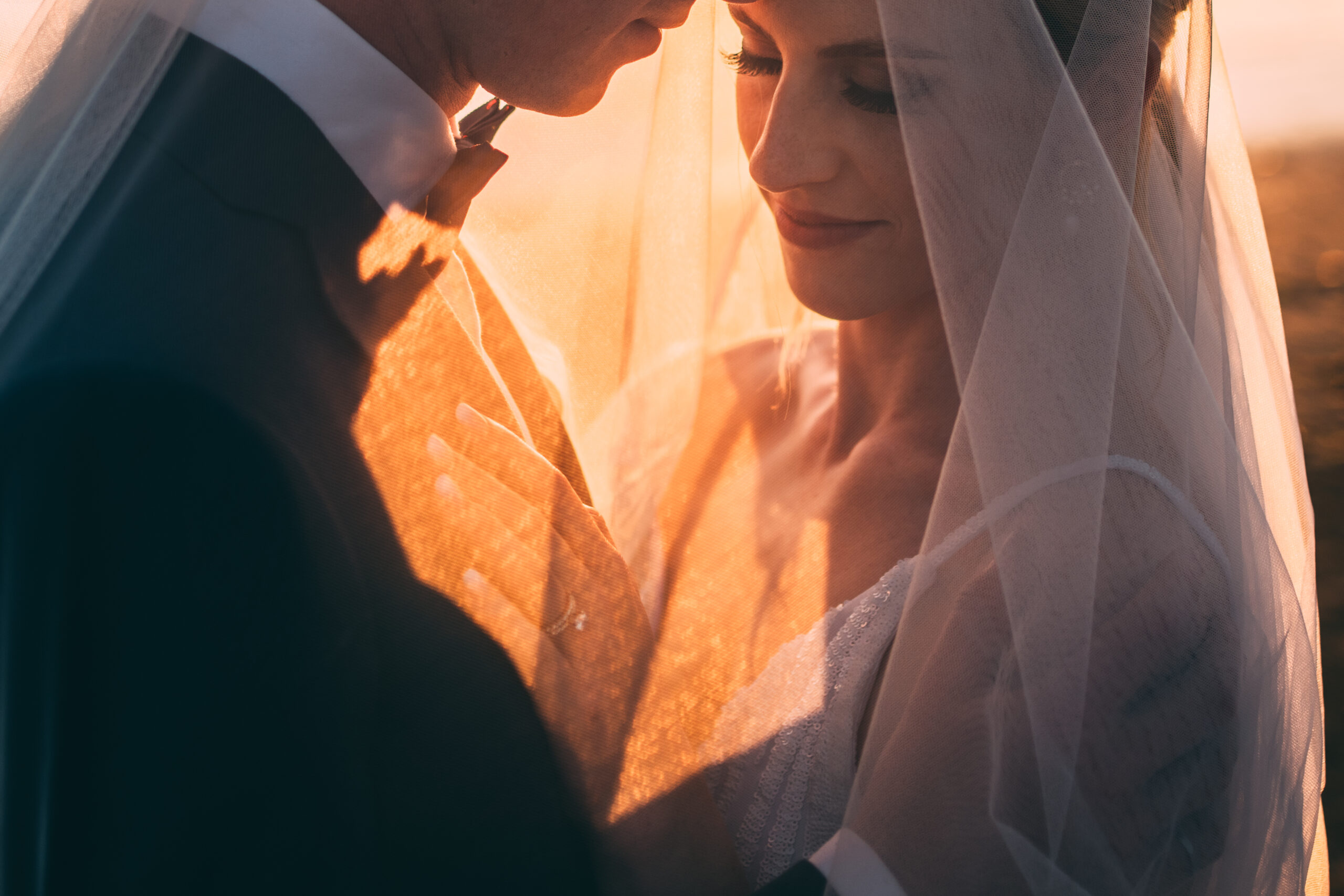 bride and groom at sunset under wedding veil